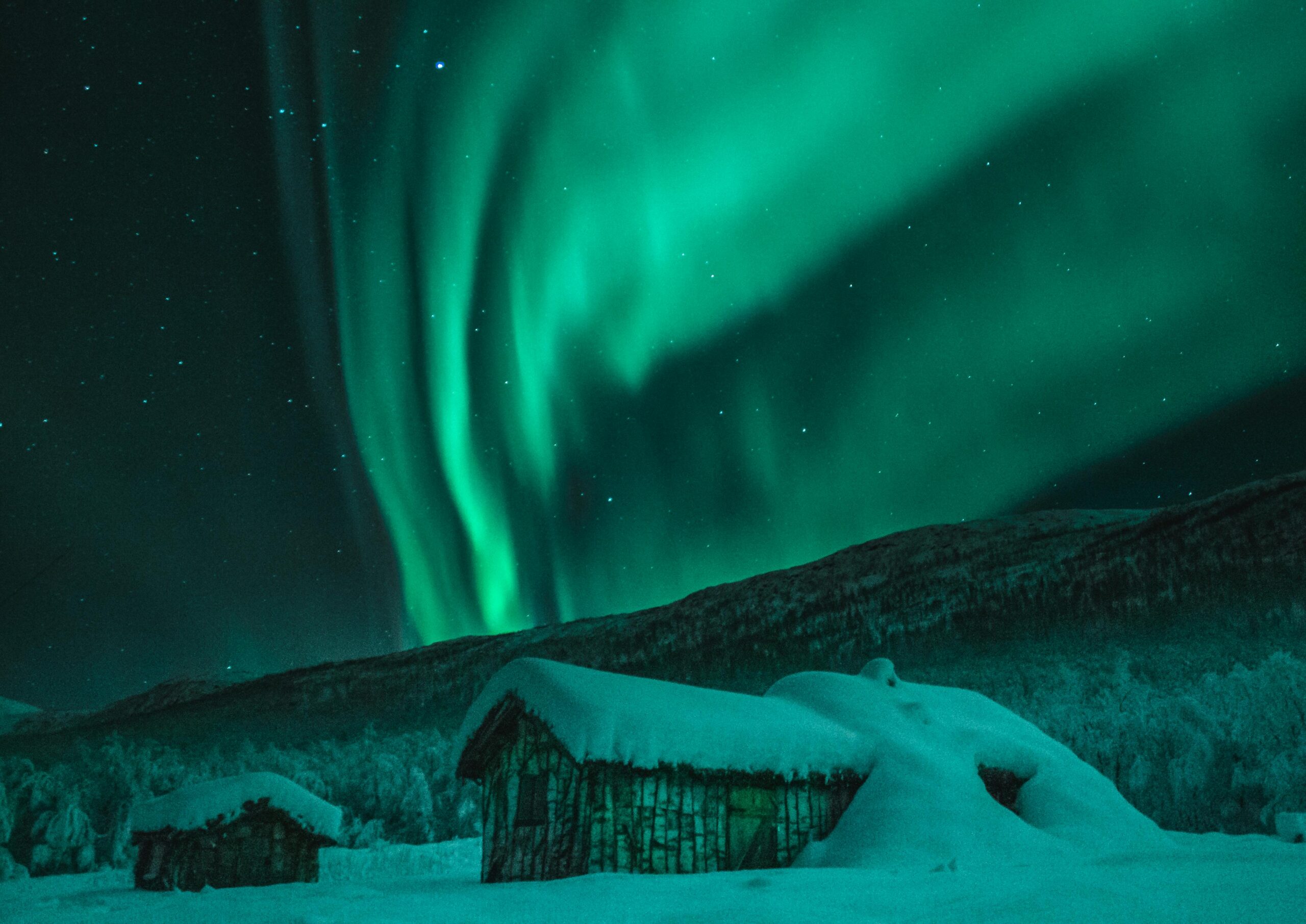 Captivating view of Northern Lights illuminating snowy cabins and wintry night sky in Norway.