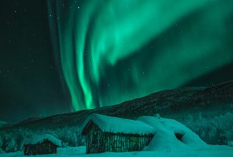pexels-photo-1674624-1674624 Captivating view of Northern Lights illuminating snowy cabins and wintry night sky in Norway.