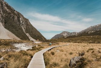 pexels-photo-808466-808466 A hiker on a tranquil boardwalk path in New Zealand's mountainous landscape under a clear sky.